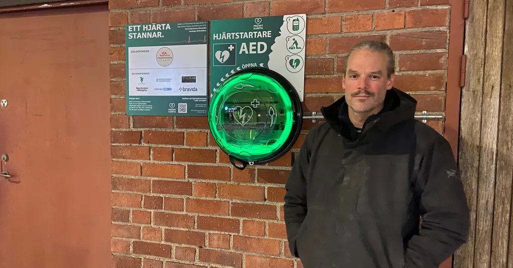 Elias Douah står bredvid den gröna utomhushjärtstartaren och Projekt Hjärtas sponsortavla i Hägerstensåsen