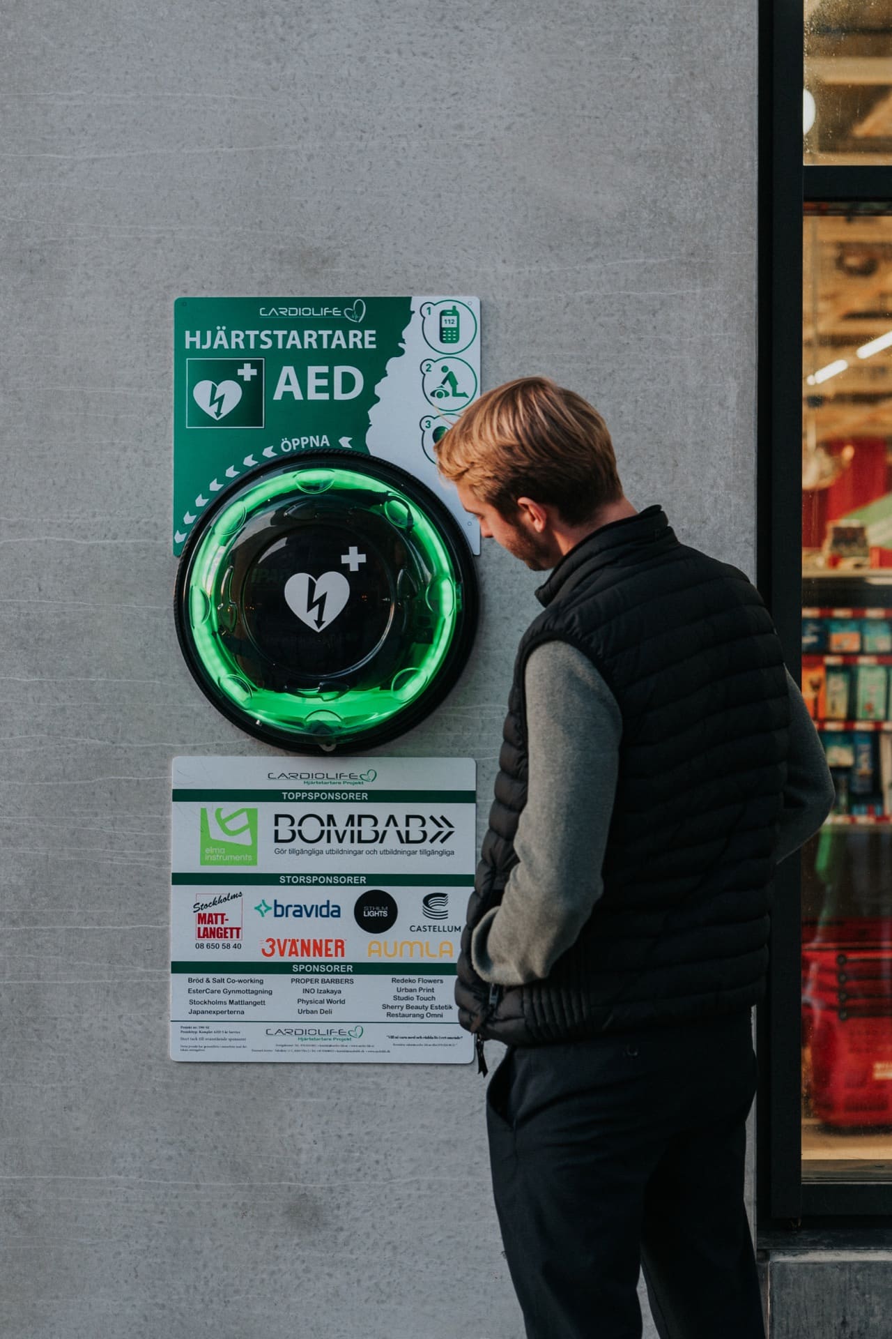 En förbipasserande stannar till vid hjärtstartarkiosken och läser sponsortavlan